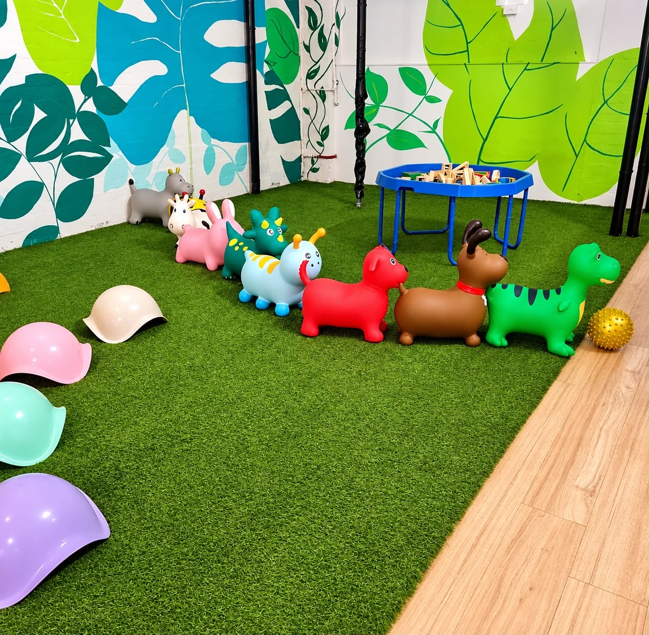 Animal hoppers and pastel stepping stones on green turf beneath a leafy wall mural