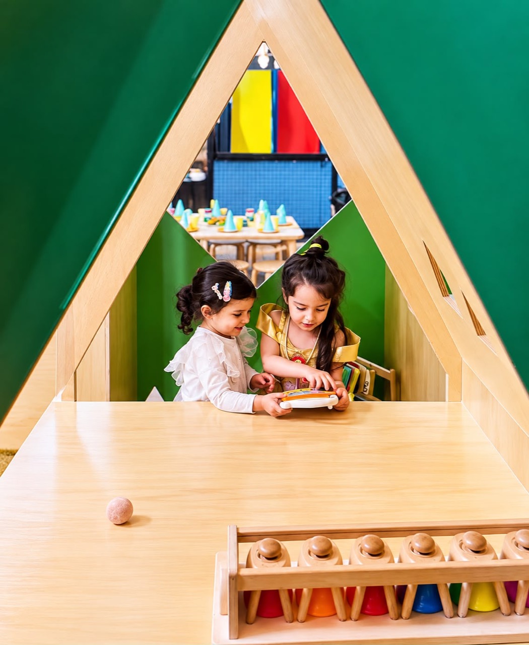 Two children playing together inside a green and timber cubby house