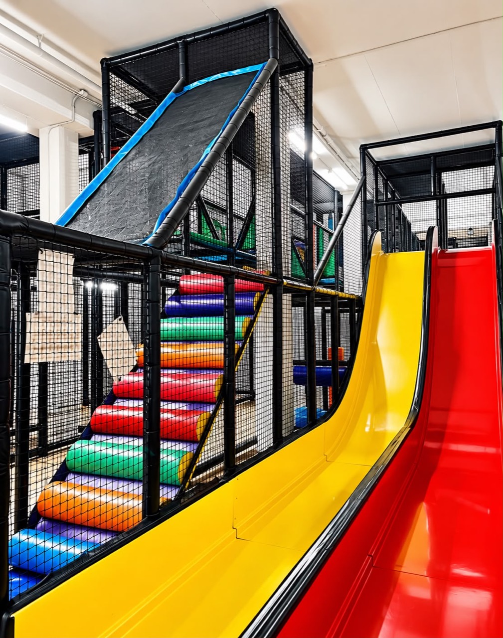 Yellow and red slides beside a climbing ramp and colourful padded steps