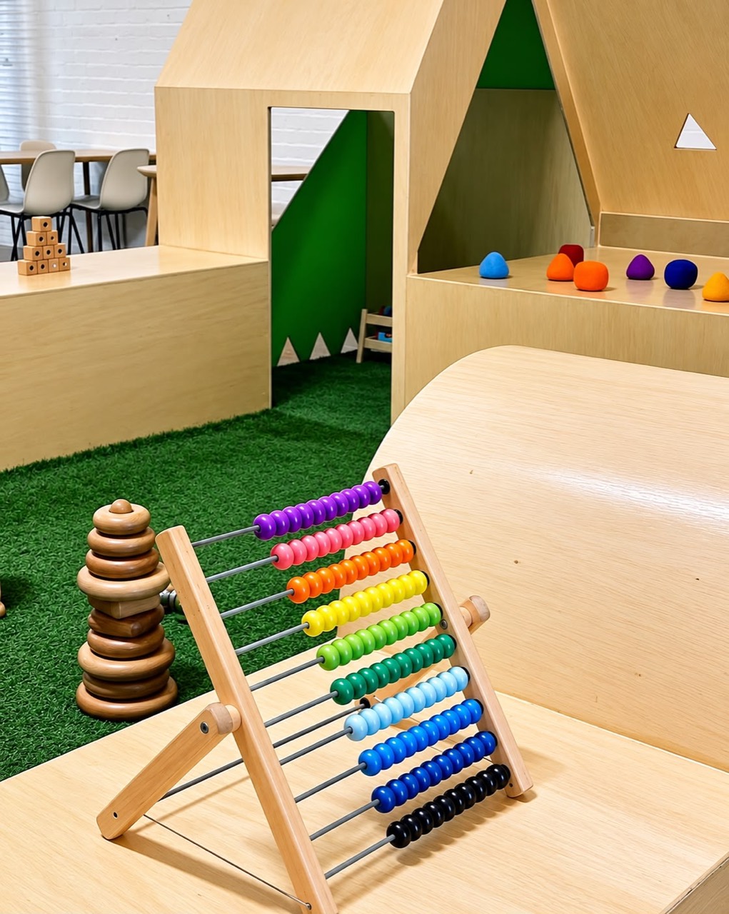 A rainbow abacus and stacking rings beside timber cubbies and colourful play stones